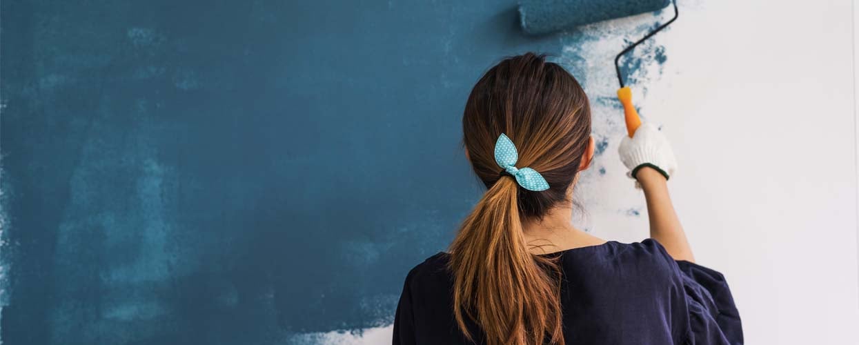 Woman painting interior wall navy blue to refresh home and increase resale appeal