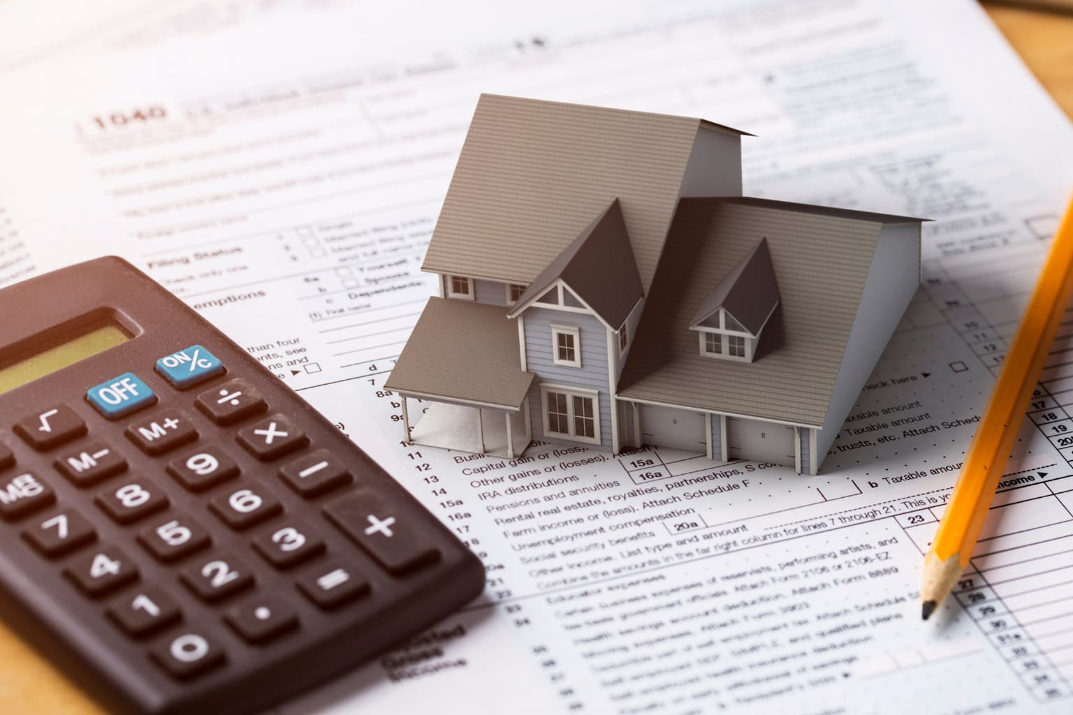 Calculator, house model, and documents showing capital gains tax for selling a home