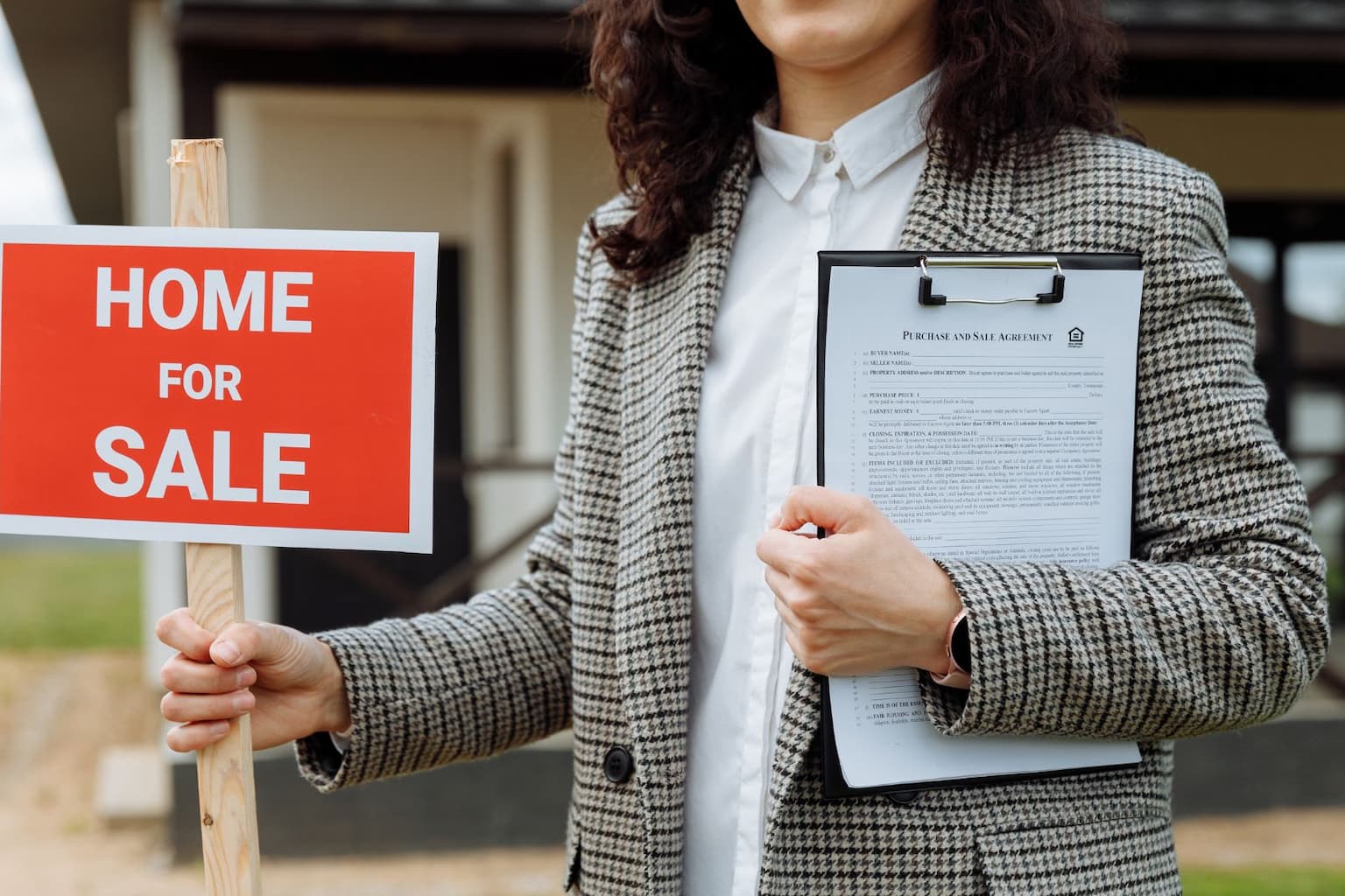 Real estate agent with “For Sale” sign in front of house