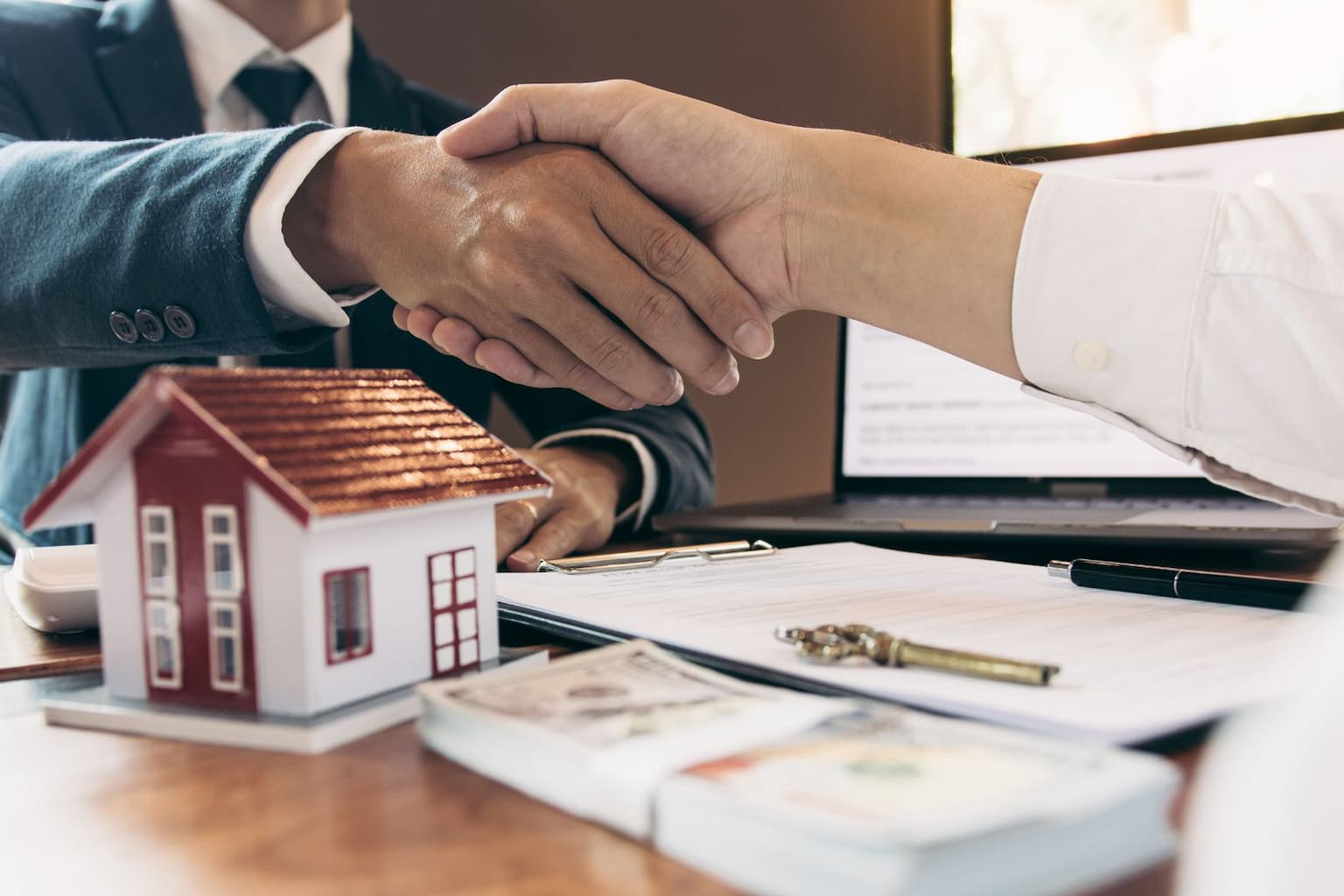 Handshake with cash and house model on desk