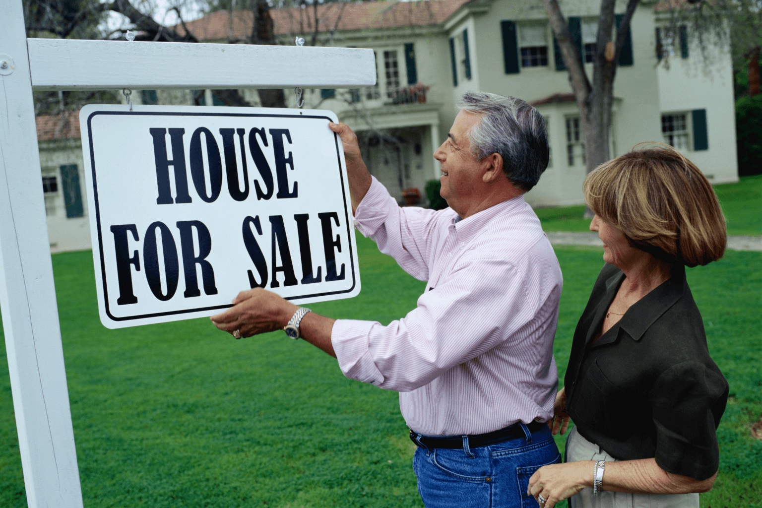 Divorced couple standing outside a house with a For Sale sign