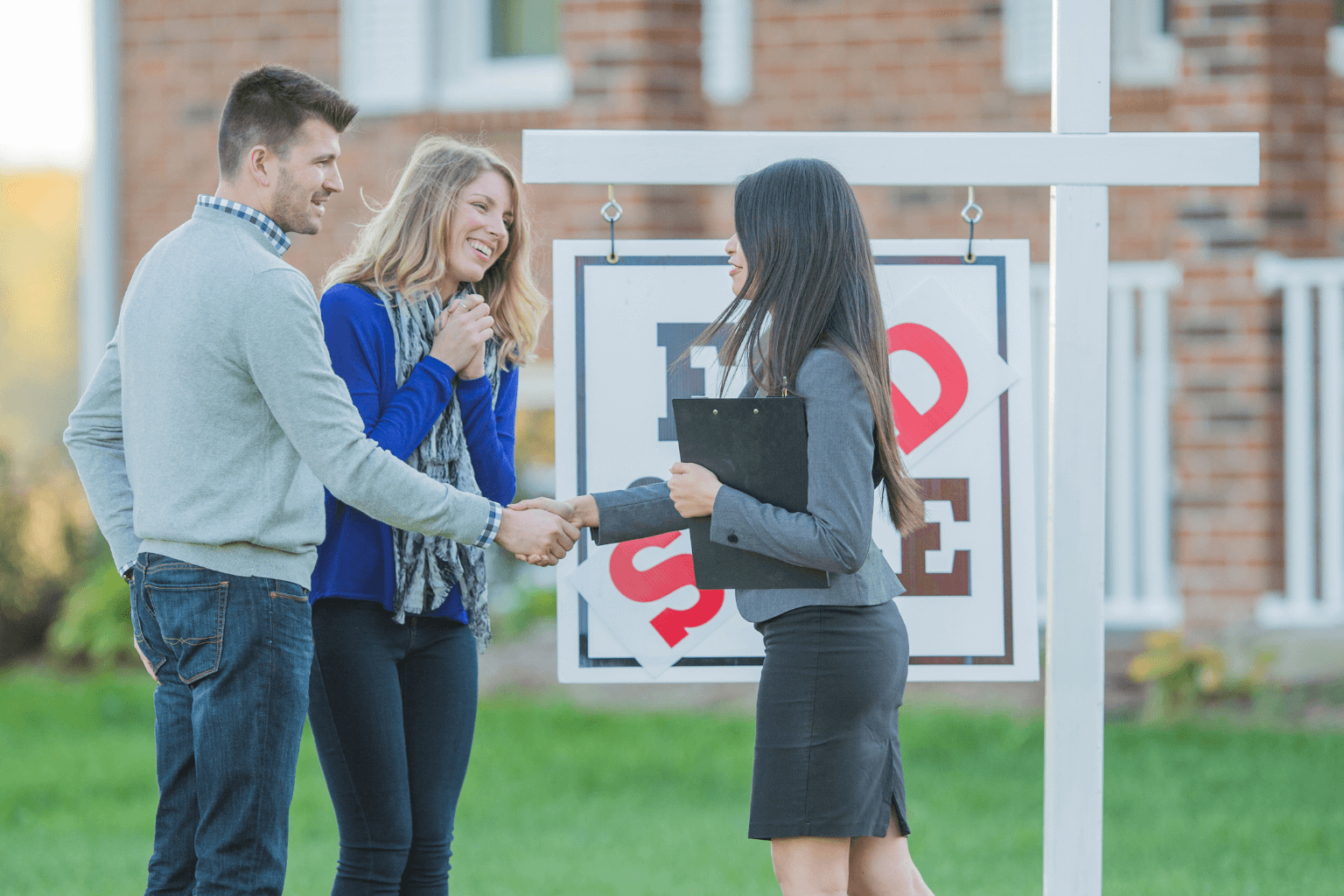 Real estate agent shaking hands with homeowner in front of house for sale