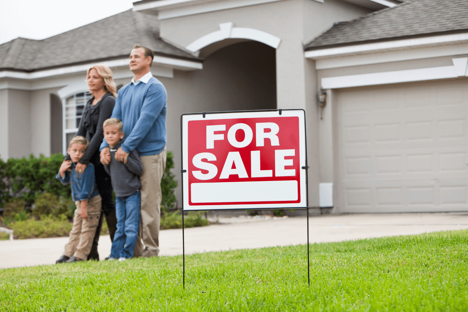 Family standing outside a house with a For Sale sign