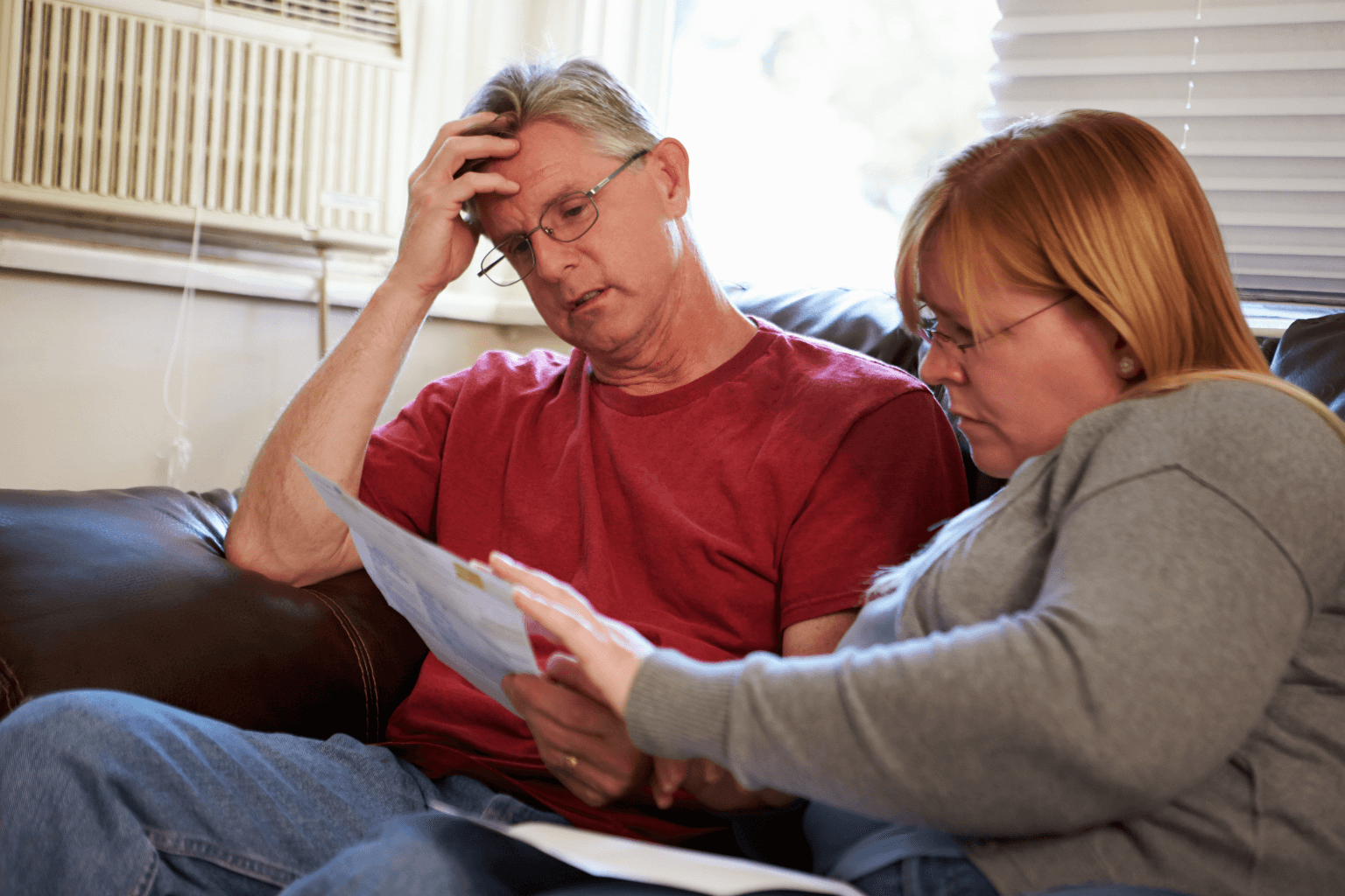 Worried couple sitting on couch looking at real estate documents