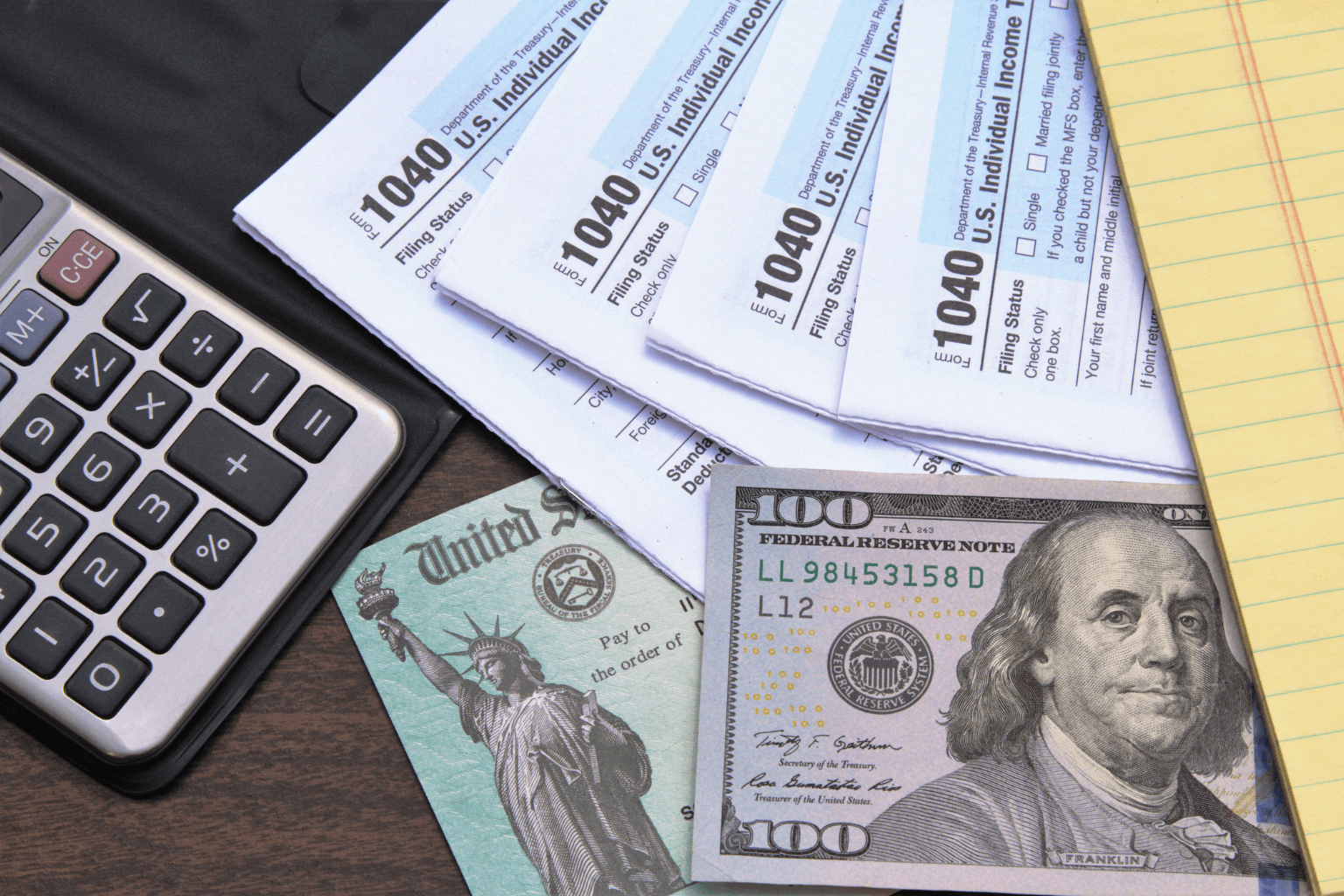 Calculator, tax forms, and money on a desk.