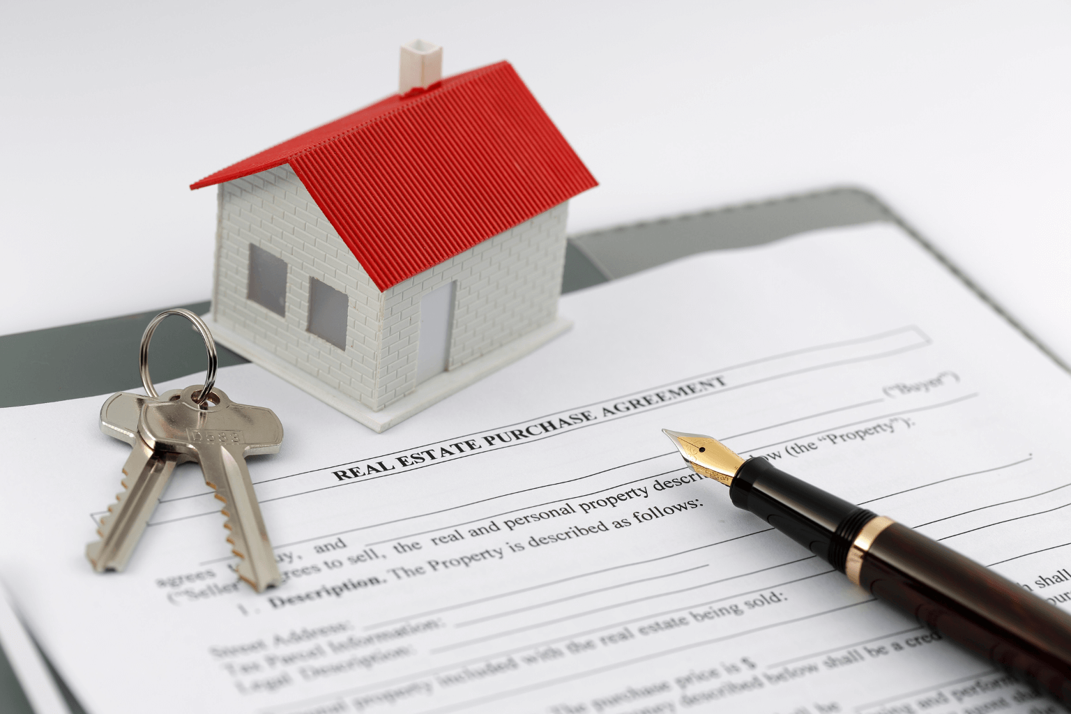A real estate contract with keys and a pen on a wooden desk
