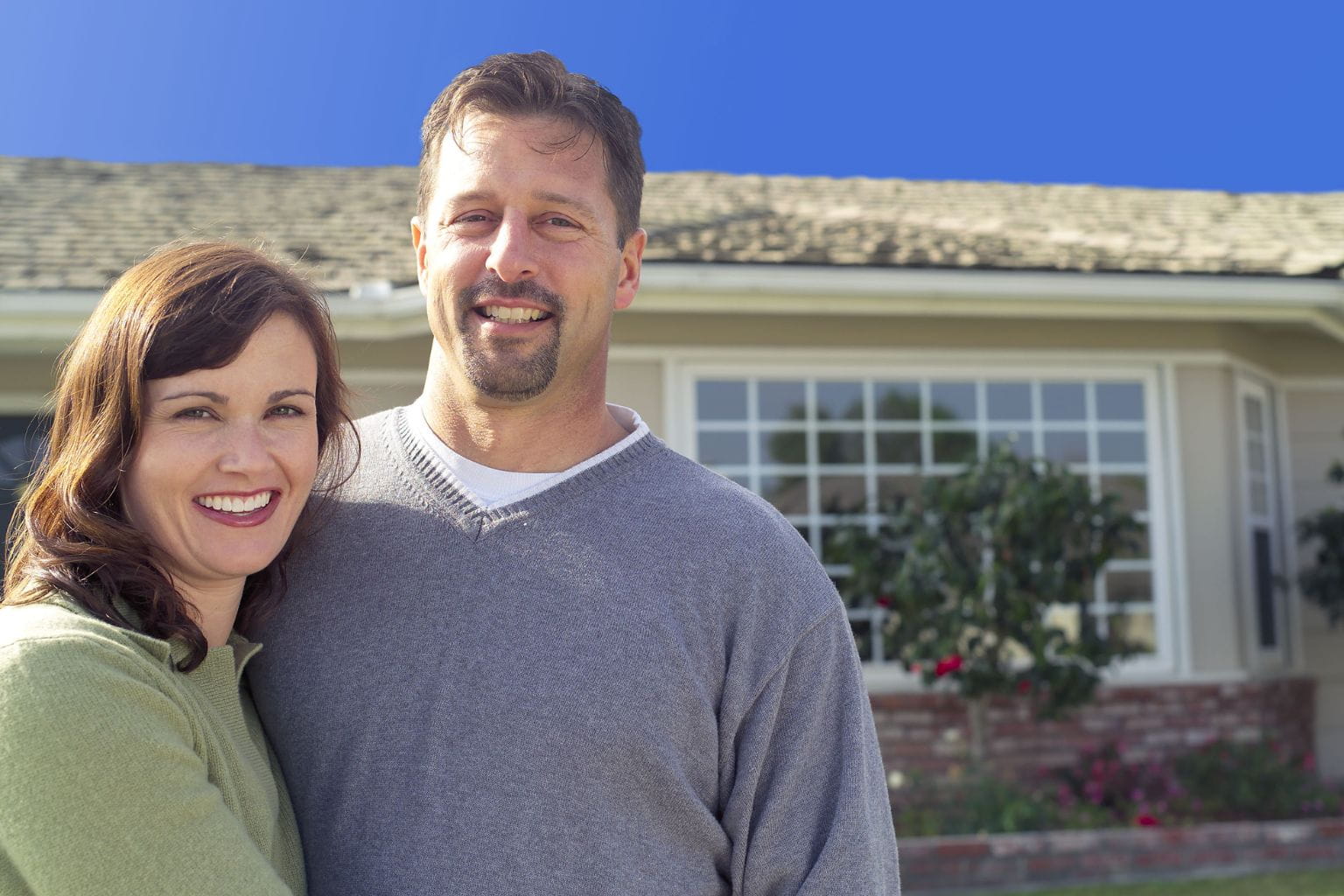 Smiling homeowners standing outside a house