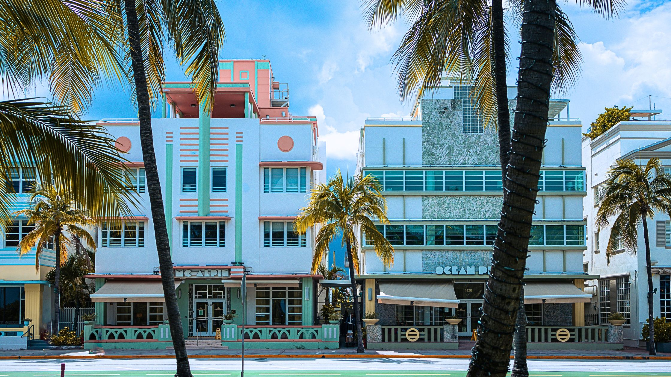 Mint green and coral Art Deco buildings along Ocean Drive in South Beach, Miami, framed by palm trees under a bright midday sky