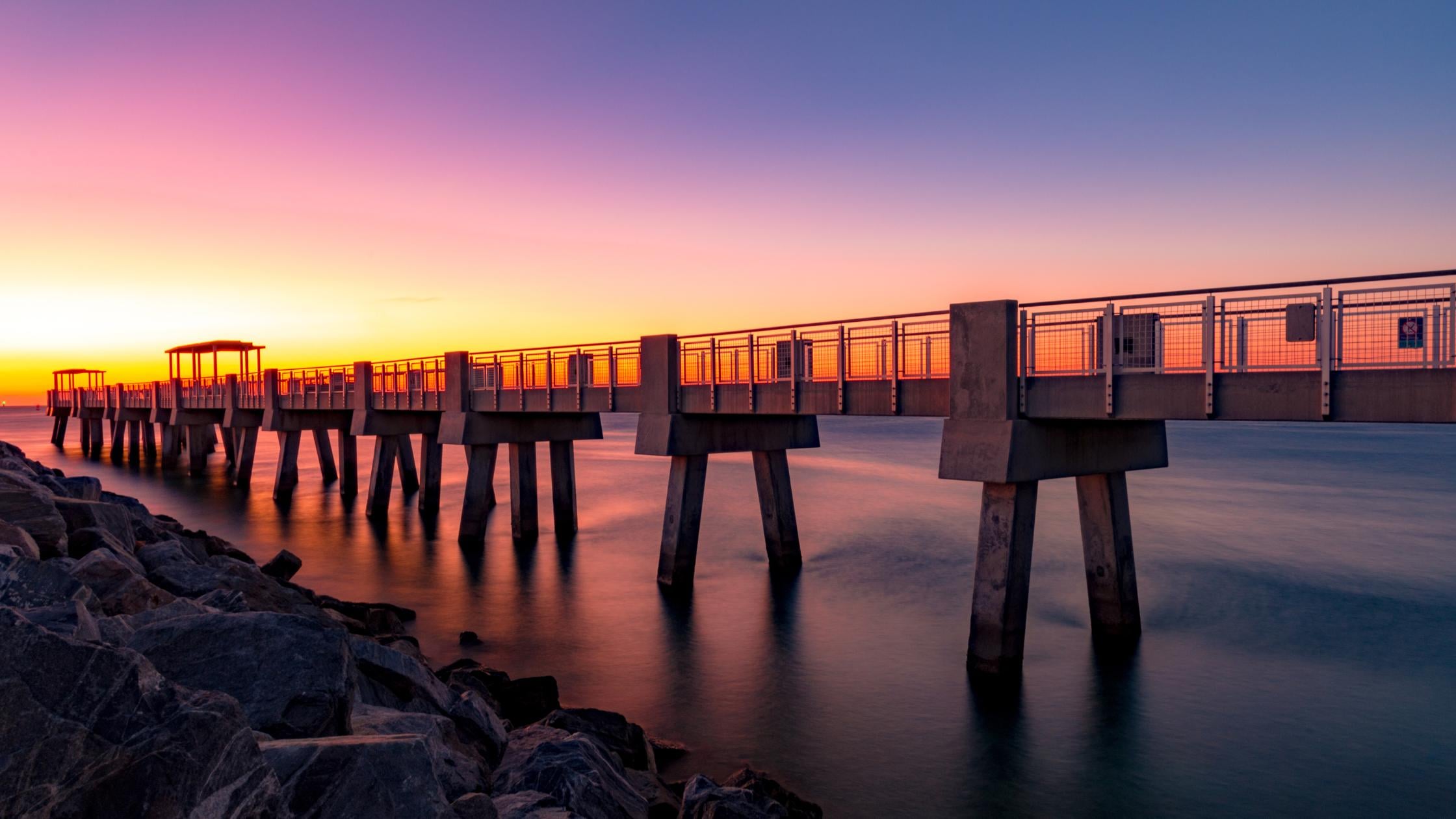 Miami waterfront pier at sunset with colorful orange and purple sky over calm water.
