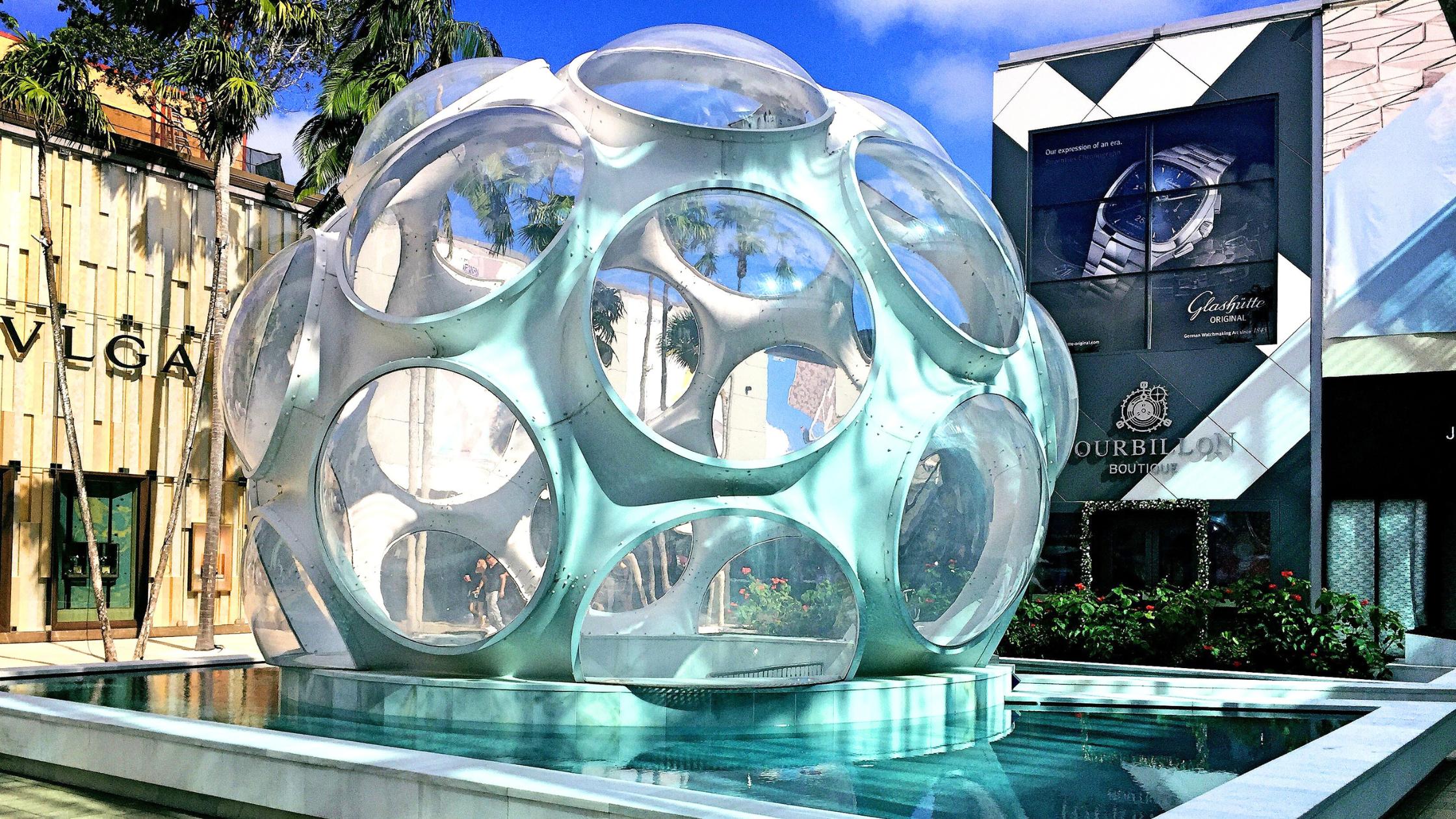 Buckminster Fuller's Fly's Eye Dome sculpture in the Miami Design District plaza, a spherical white geodesic structure reflected in a surrounding pool