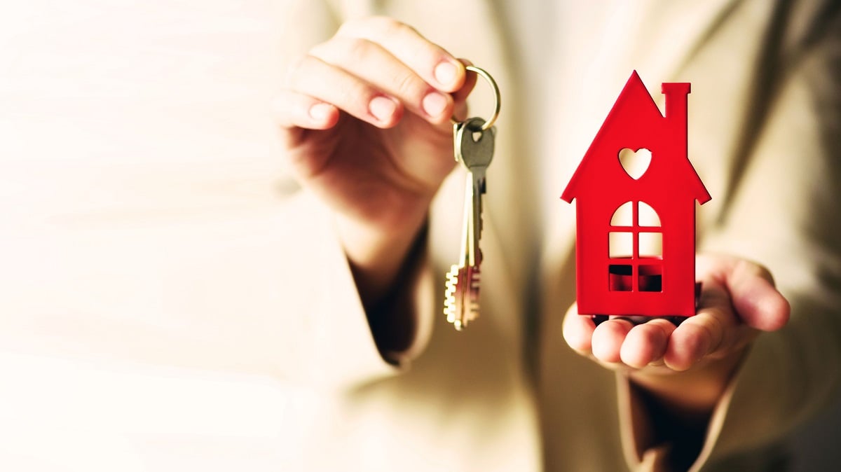 Female hands holding small red house and keys.