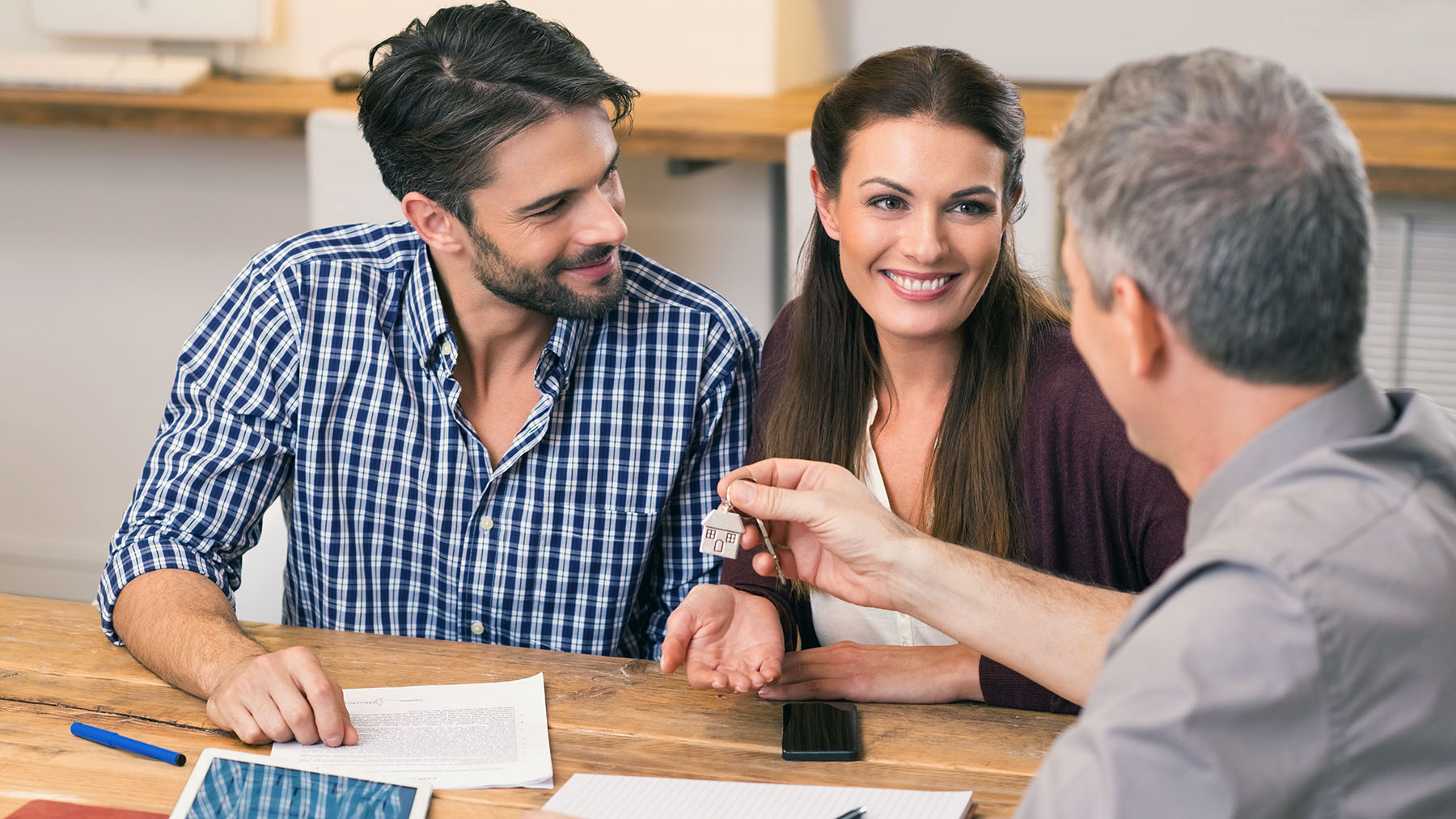 Young happy couple receiving house keys from real estate agent. Giving keys of new house to young couple. Smiling couple signing financial contract for mortgage.