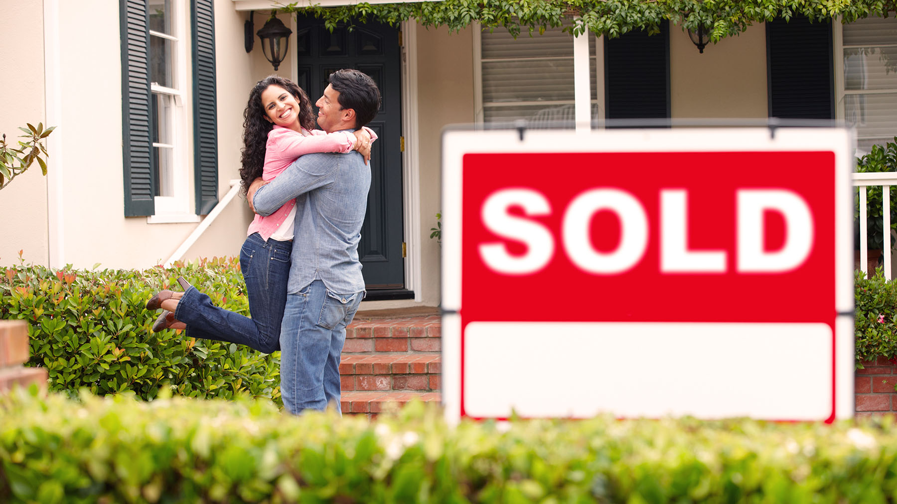 Hispanic couple outside home with sold sign