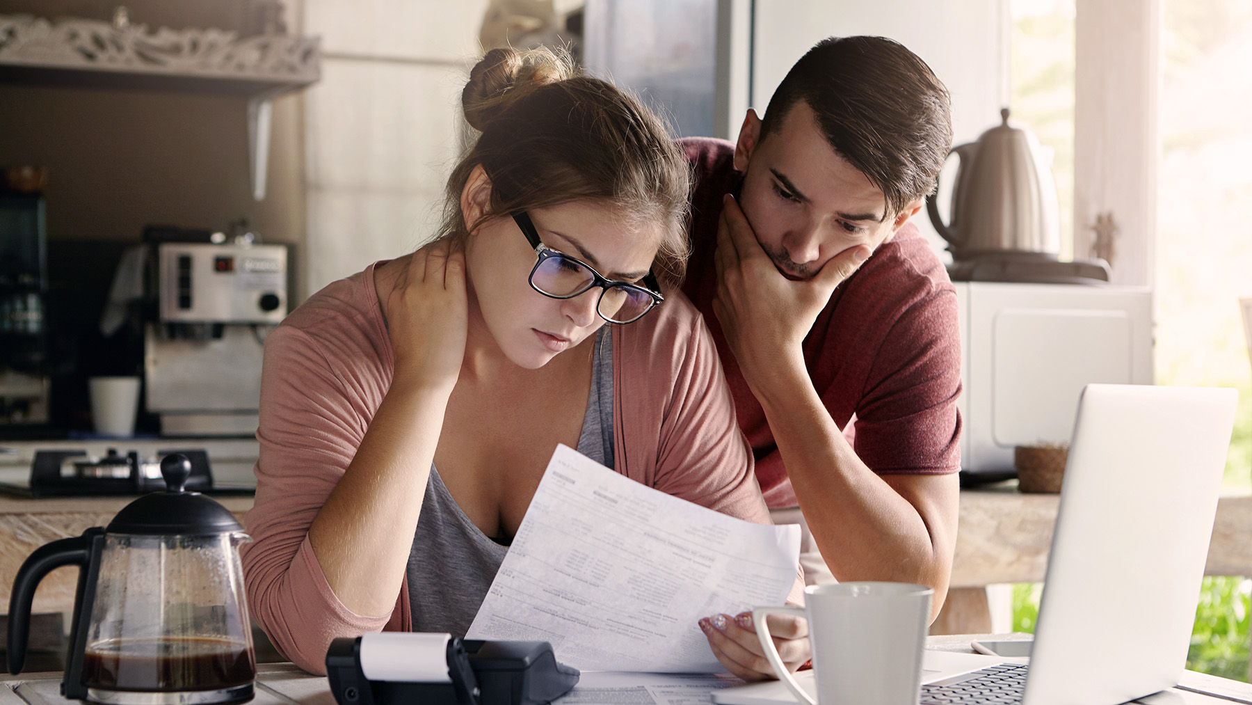 Young Caucasian family having debt problems, not able to pay out their loan. Female in glasses and brunette man studying paper form bank while managing domestic budget together in kitchen interior