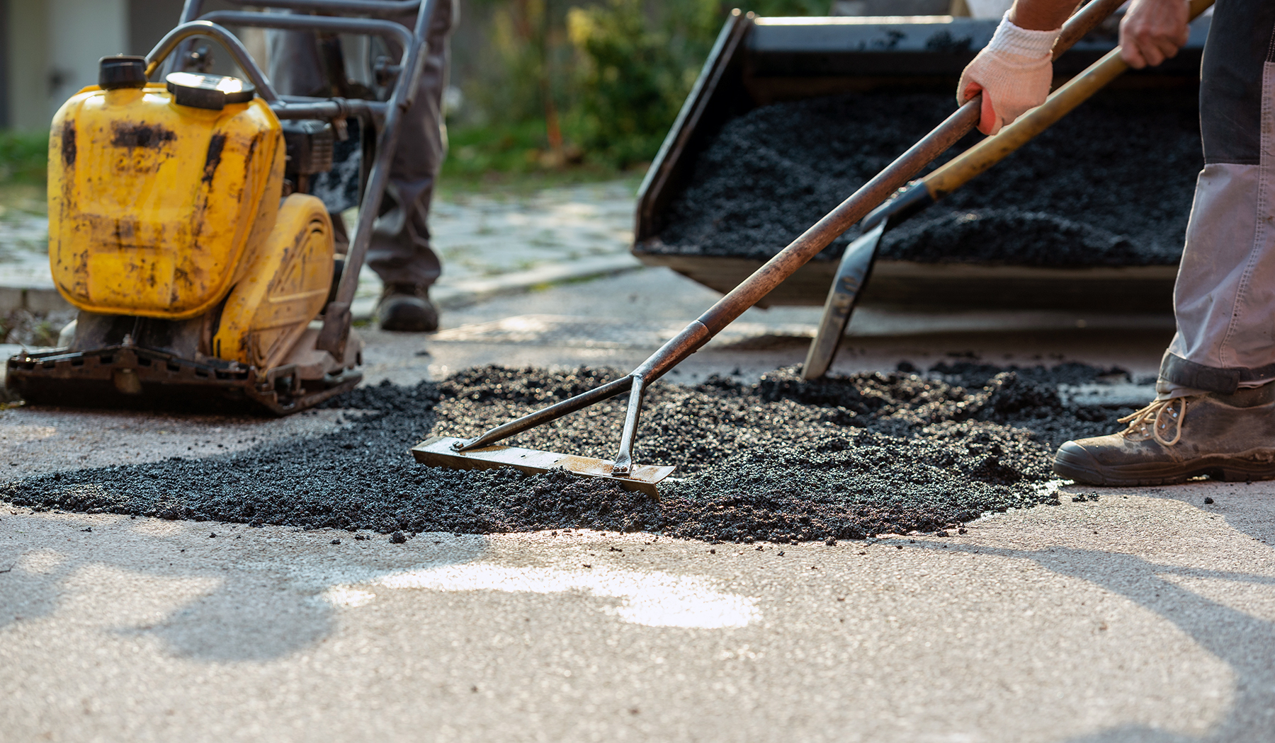 Low angle view of two workers arranging fresh asphalt mix with r
