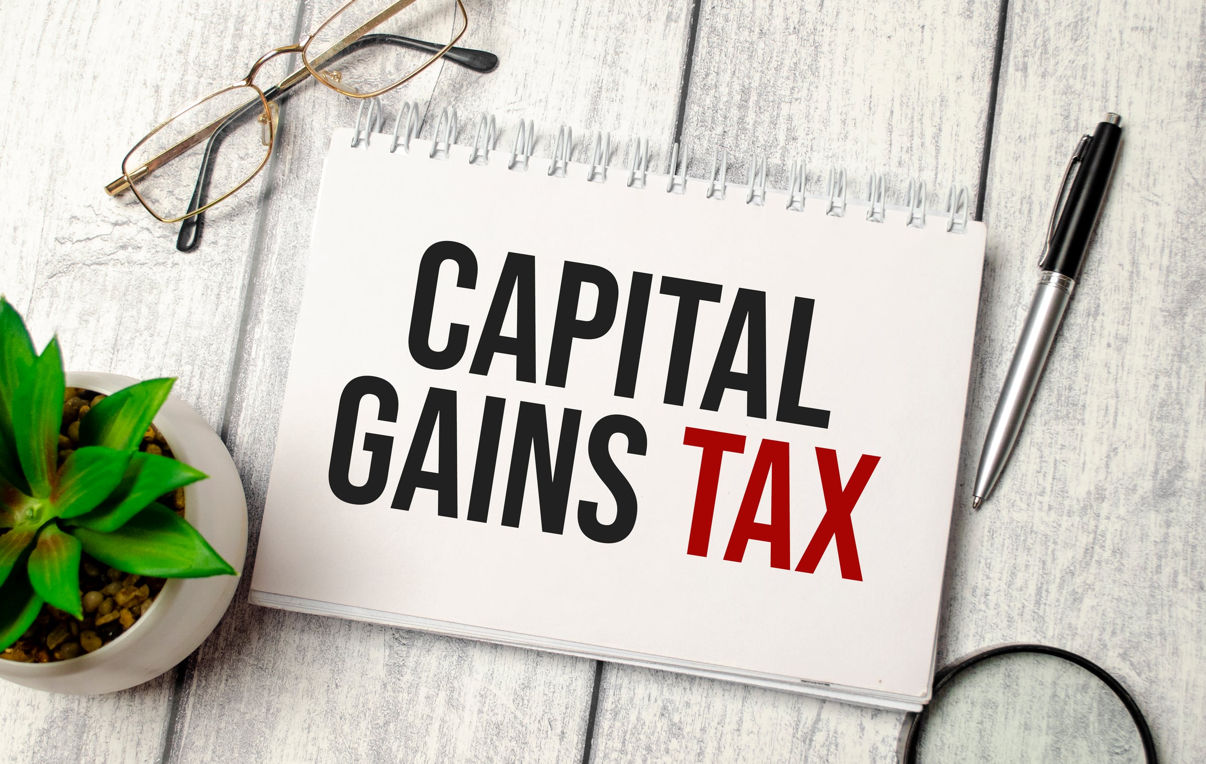capital gains tax words on notebook and pen, glasses and magnifier