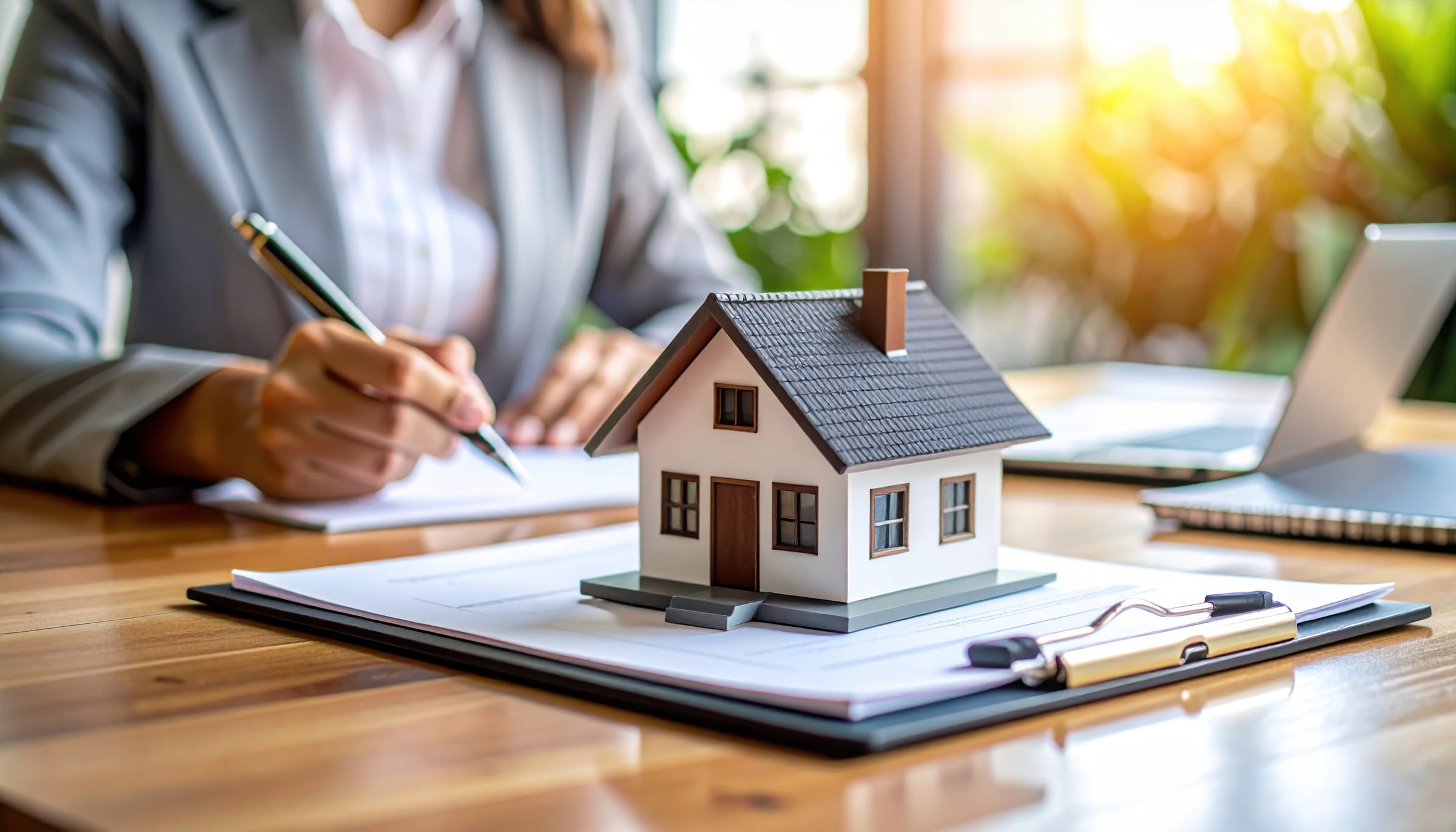 House model sits proudly on desk of real estate agent, surrounded by neatly organized documents and laptop, creating professional atmosphere for client interactions