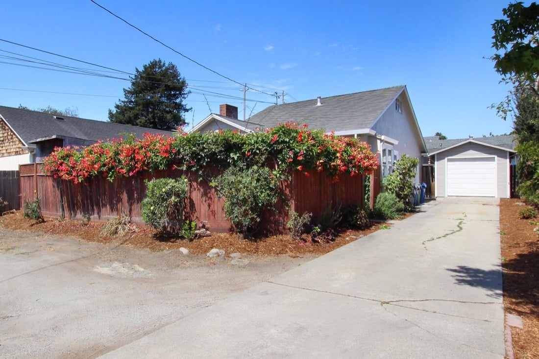 Front of the property: a long concrete driveway beside a wood fence covered in red bougainvillea, leading to a one-car garage