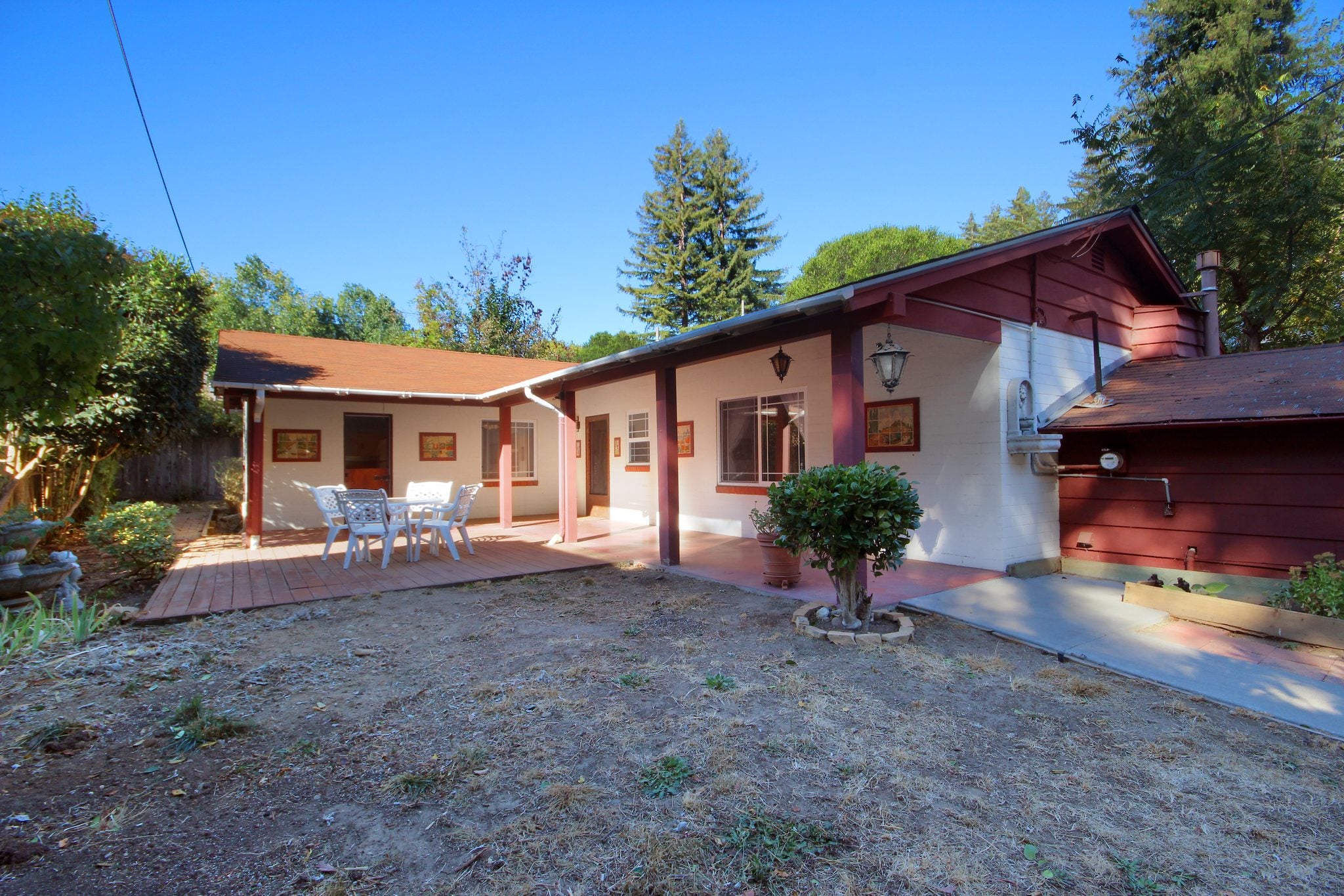 Front of the house, a single-story home with a courtyard and patio set under redwoods