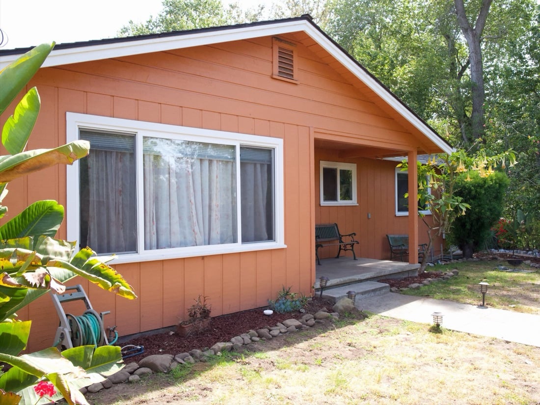 Front of the house: orange wood-sided single-story home with a small porch and garden