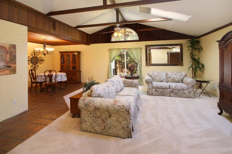 Staged living room with vaulted wood-beam ceiling, floral sofas and a dining area beyond