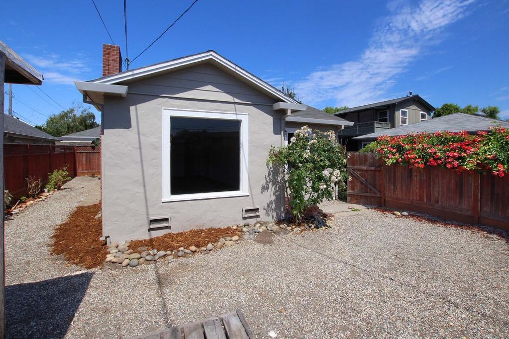 House exterior in taupe with white trim, gravel yard and garden beds