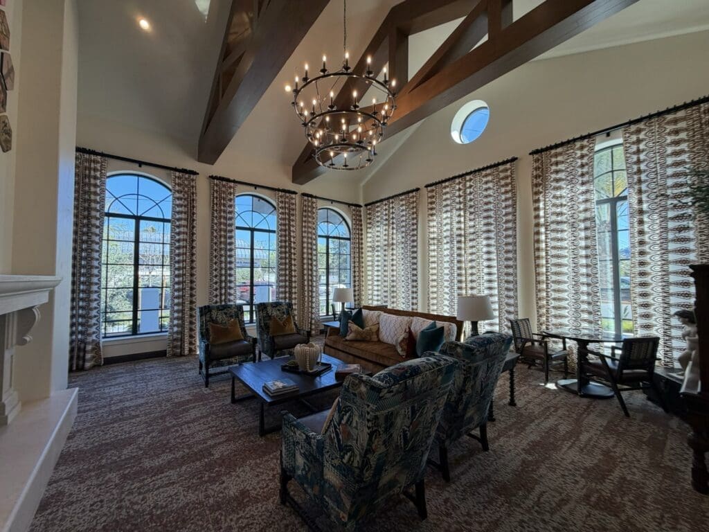 Main living room at Aegis Living San Rafael with a vaulted wood-beamed ceiling, iron chandelier, tall arched windows and patterned upholstered armchairs
