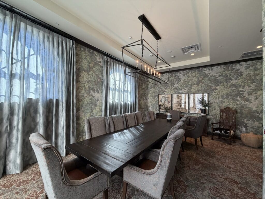 Private dining room at Aegis Living San Rafael with a long wood table, upholstered chairs, botanical wallpaper and a linear candle chandelier