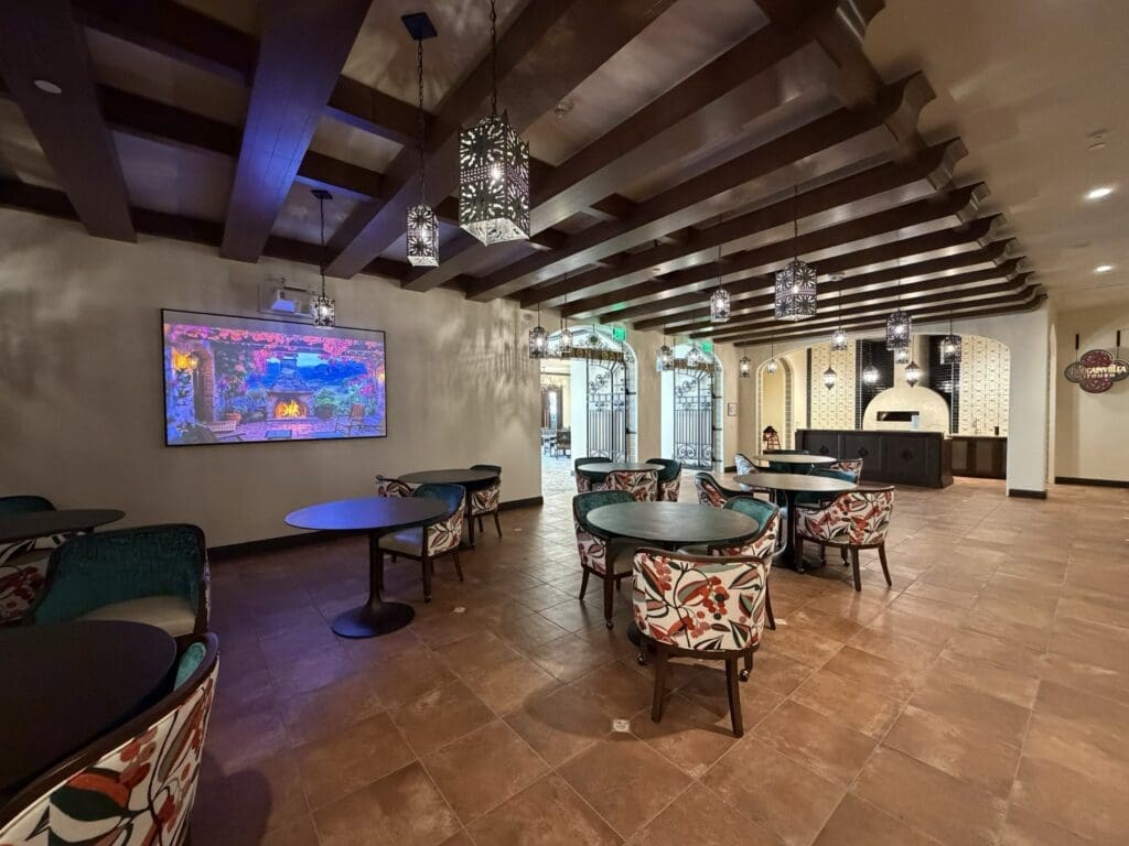 Bistro area at Aegis Living San Rafael with café tables, a wall screen showing a fireplace scene and the tiled pizza oven counter in the background