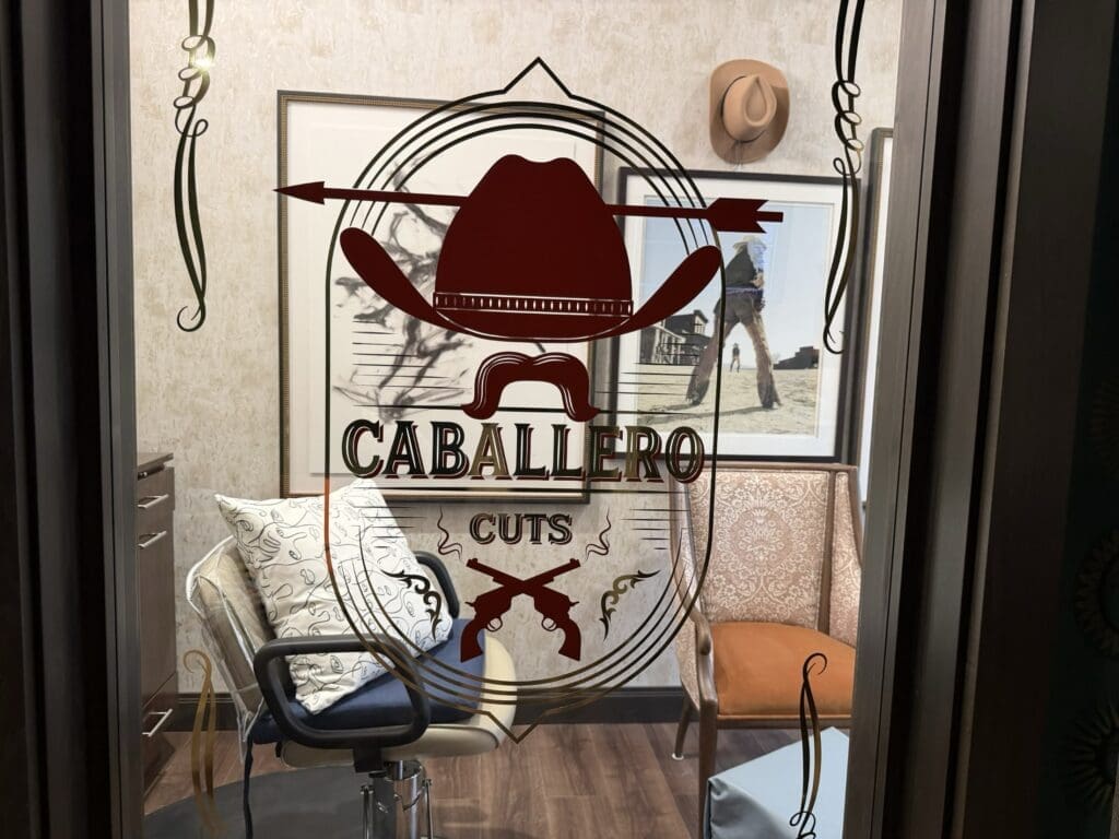 Glass door of the Caballero Cuts barbershop at Aegis Living San Rafael with a cowboy hat logo and a salon chair inside