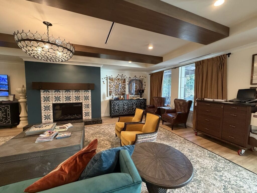 Third-floor living room at Aegis Living San Rafael with a tiled fireplace, teal sofa, mustard armchairs, leather wingback chairs and a beaded chandelier