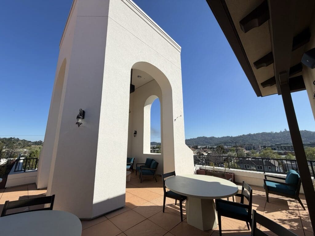 Fifth-floor Vista Terrace at Aegis Living San Rafael with outdoor tables beside the arched white bell tower and views of the Marin hills