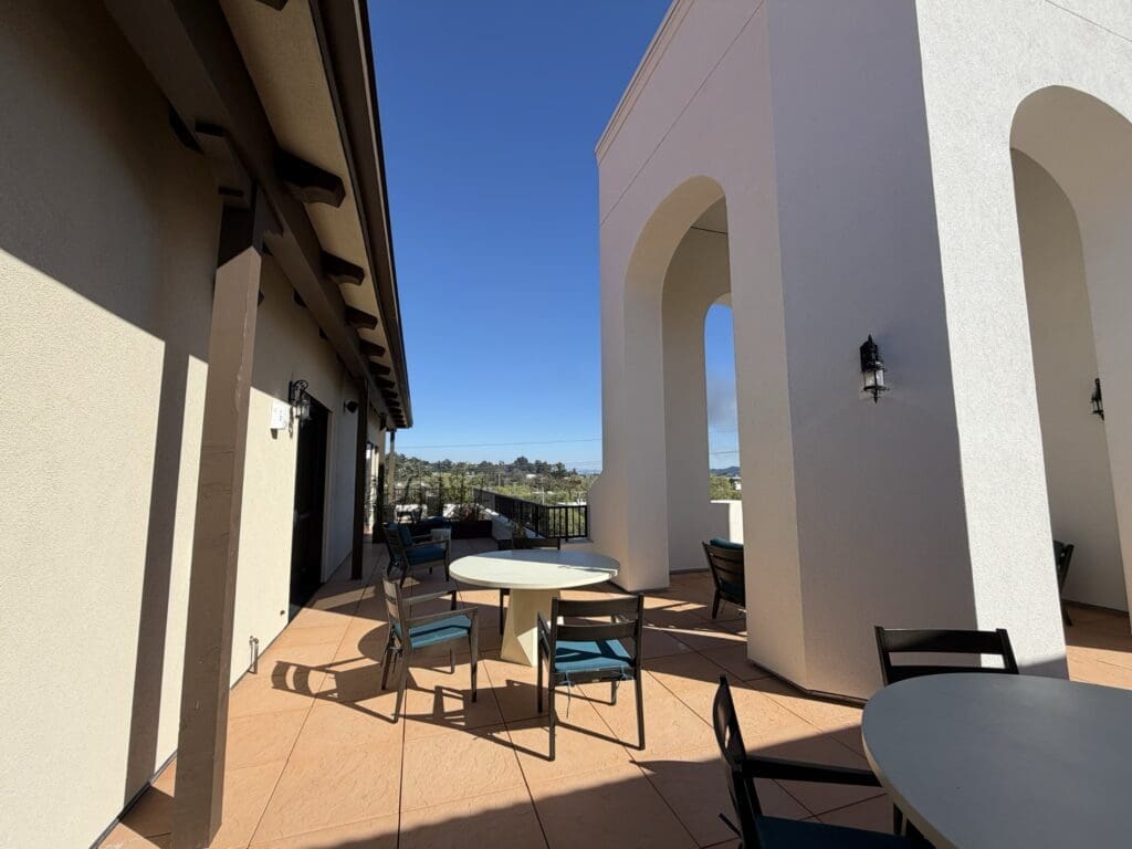 Covered walkway and patio seating on the rooftop terrace at Aegis Living San Rafael under a clear blue sky
