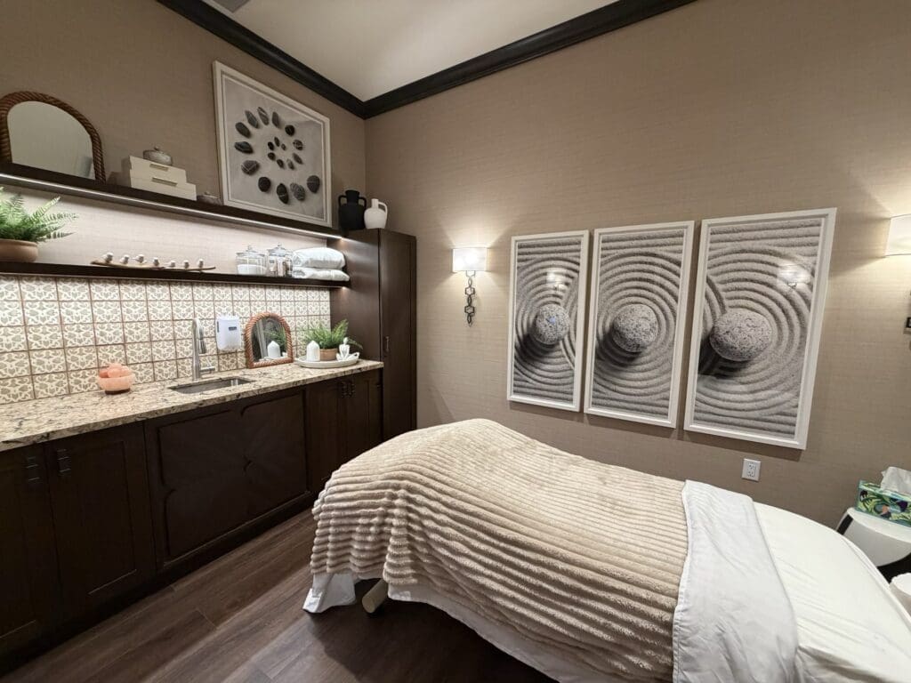Massage room at Aegis Living San Rafael with a treatment table, tiled sink counter, floating shelves and three framed zen garden prints