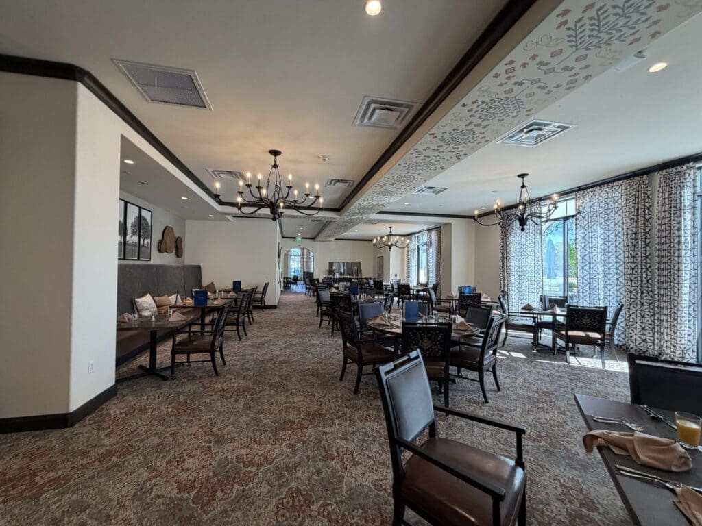 Main dining room at Aegis Living San Rafael with set tables, iron chandeliers, a painted ceiling panel and windows with patterned drapes