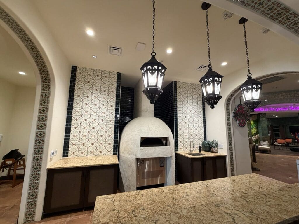 Domed wood-fired pizza oven framed by patterned Spanish tile and iron lanterns in the bistro at Aegis Living San Rafael