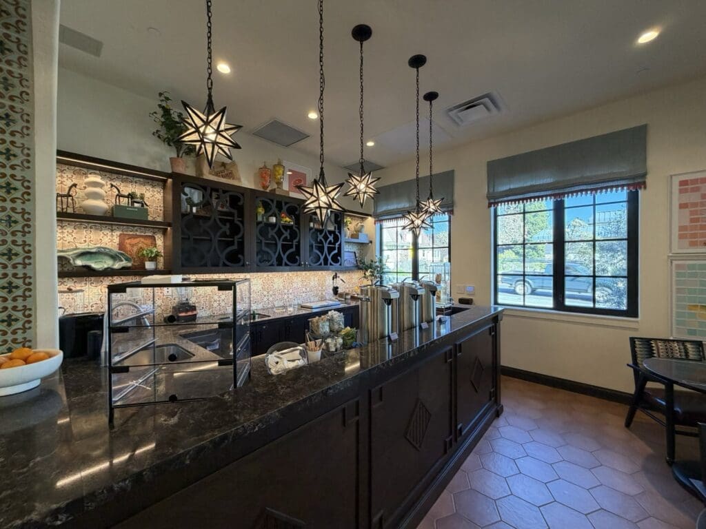 Coffee and juice bar at Aegis Living San Rafael with star-shaped pendant lights, a dark granite counter, beverage dispensers and a patterned tile backsplash