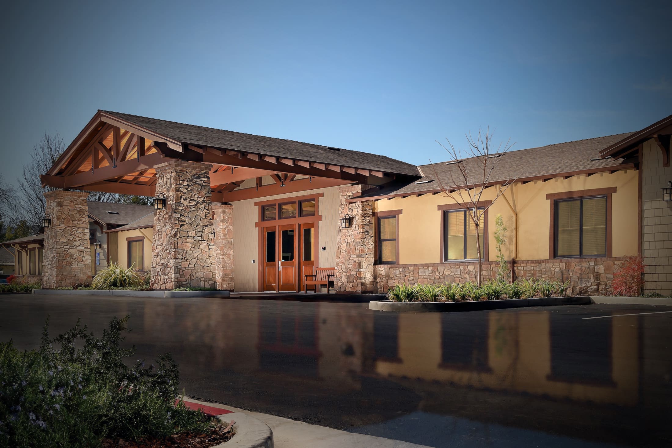 Front entrance of Sunol Creek Memory Care in Pleasanton, a single-story Craftsman-style building with stone columns and a timber porte-cochere
