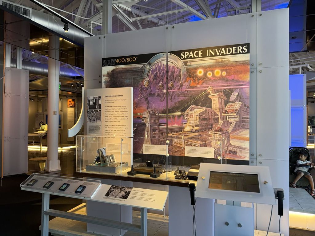 Atari 400 and 800 home computers and Atari 2600 console beneath Space Invaders artwork in the video game exhibit at the Computer History Museum