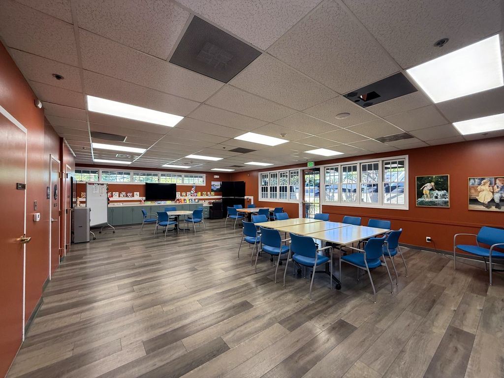 Program room with an arts and crafts counter, a TV, original paintings and garden-view windows at Hearts & Minds Activity Center in San Jose