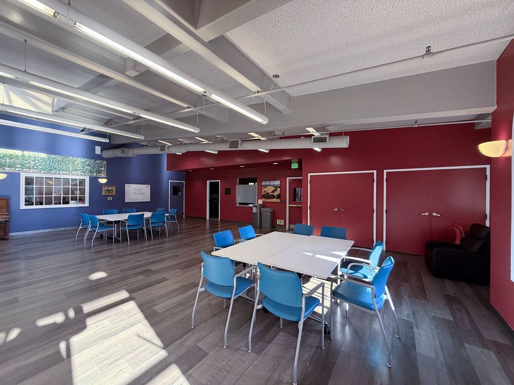Main activity room with red and blue walls, a piano and tables set for small groups at Hearts & Minds Activity Center in San Jose