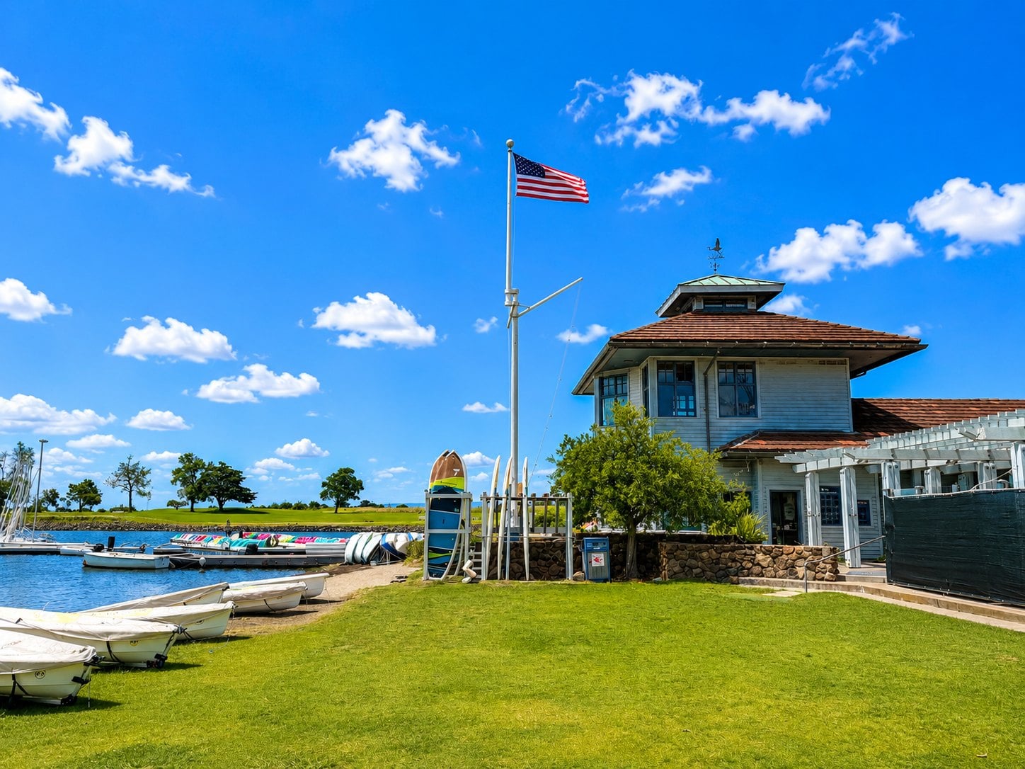 Shoreline Lake Boathouse in Mountain View with its cupola, American flag on a nautical mast, and paddleboards and sailboats on the lawn