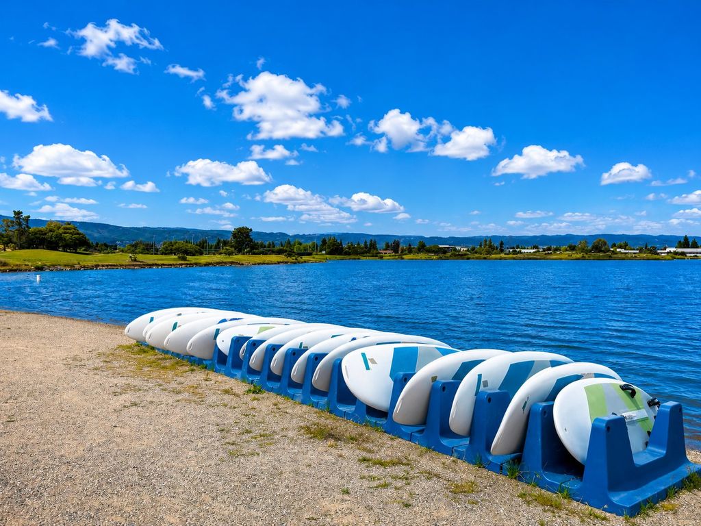 Rental stand-up paddleboards stacked in blue racks along the beach at Shoreline Lake in Mountain View
