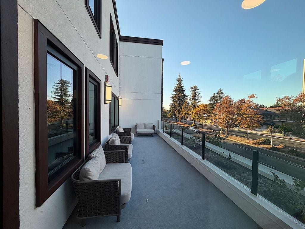 Balcony with glass railing and outdoor lounge chairs overlooking El Camino Real at Villa Toscana Memory Care in Mountain View