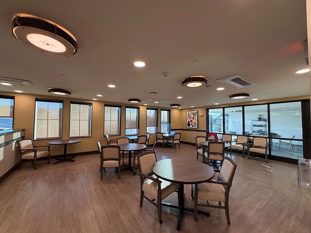 Memory care dining room with round tables and windows opening to the patio at Villa Toscana Memory Care