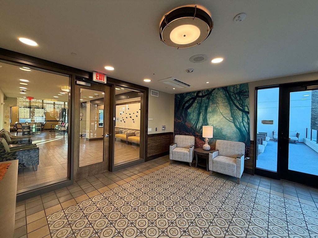 Memory care neighborhood entry lounge with forest mural, armchairs and patio door at Villa Toscana
