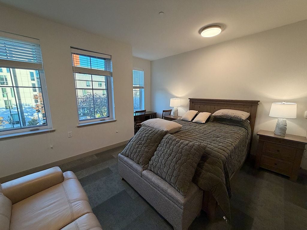 Furnished private suite with queen bed, nightstands and three windows at Villa Toscana Memory Care