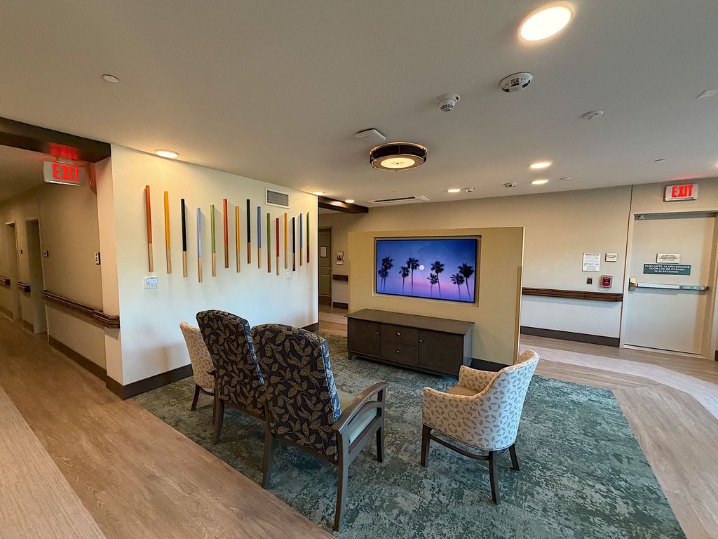 TV lounge with high-back chairs and colorful wall art in a memory care neighborhood at Villa Toscana