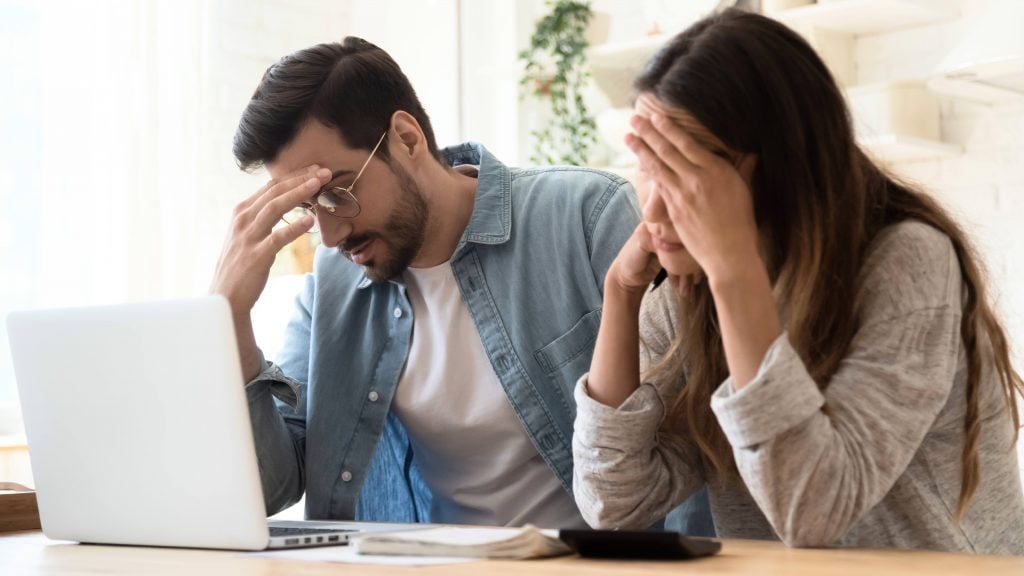 a-young-couple-a-white-man-and-a-white-woman-sitting-together-at-a-kitchen-table-looking-stressed-sad-worried-while-working-on-a-computer-16x9-1-1024x576
