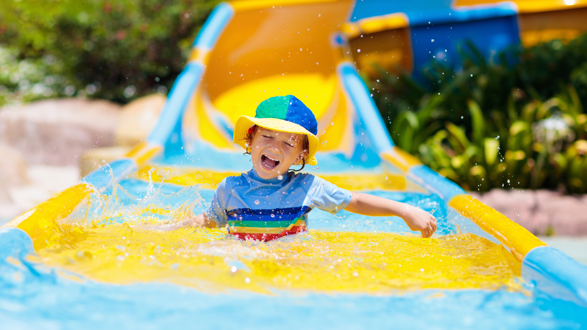 Smiling child splashing at bottom of colorful water slide